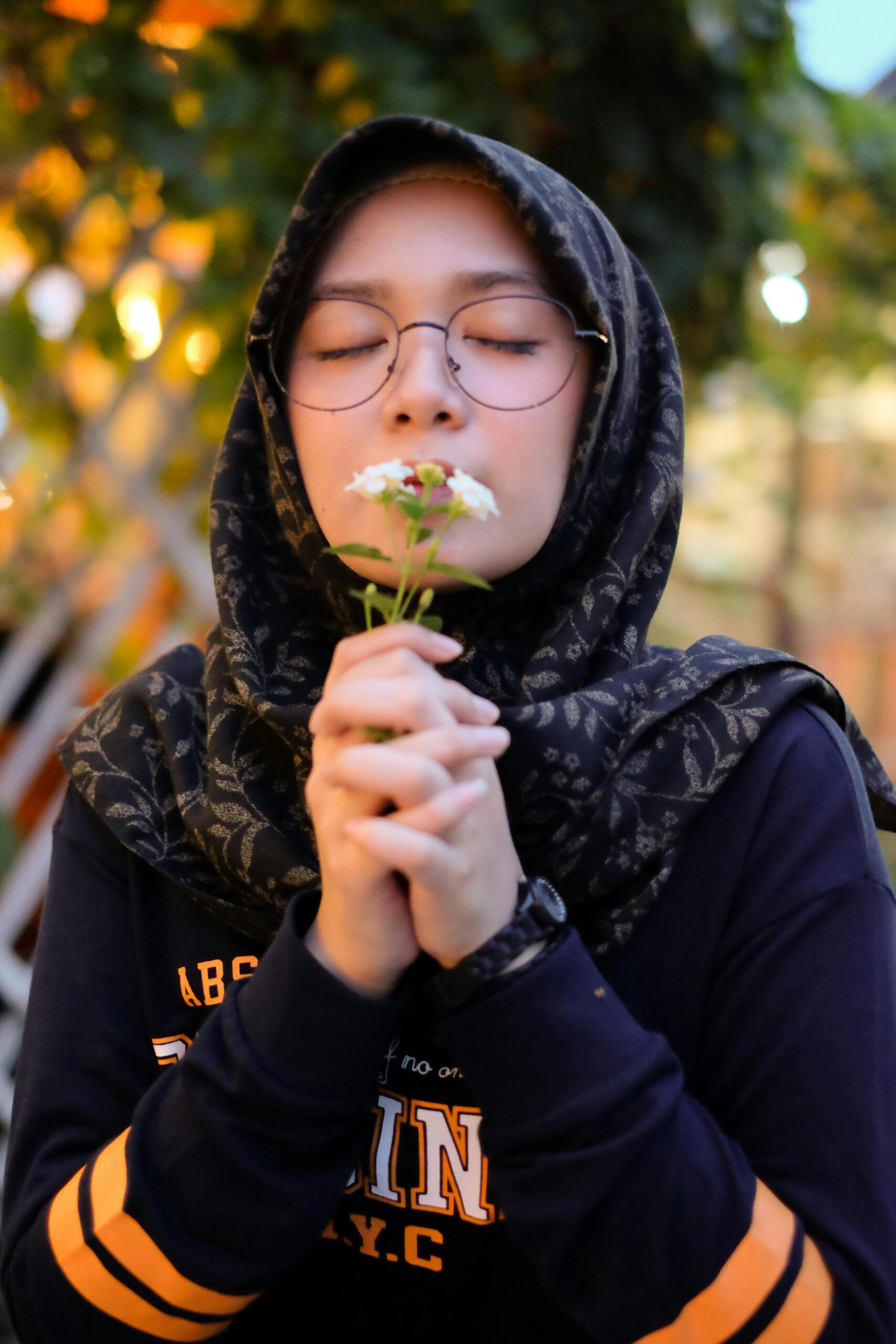 A serene portrait of a young woman in a hijab savoring the scent of a flower outdoors.